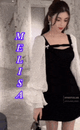 a woman in a black dress with white sleeves is standing in front of a wall that says melissa