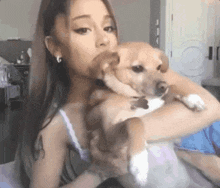 ariana grande is holding a small brown dog in her arms and kissing it .