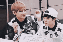 two young men are sitting next to each other and one of them is wearing a white shirt with the letters gg on it