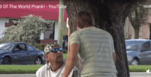 a man is sitting under a tree talking to a woman who is standing next to him ..