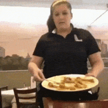 a woman in a black shirt with the letter l on it is serving a plate of food .