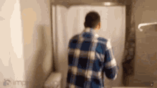 a man in a plaid shirt is standing in a bathroom looking at himself in a mirror .