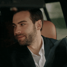 a man with a beard and a suit is sitting in the back seat of a car