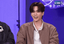 a man in a brown jacket is smiling in front of a sign that says g-mm