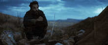 a man with a beard is kneeling down in a field with a sword in his hand
