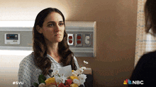 a woman in a hospital gown holds a bouquet of flowers in front of a nbc logo