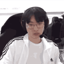 a young man wearing glasses and a white adidas jacket is sitting in a chair .