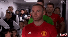 a man in a red shirt is standing in front of a crowd of people in a dressing room .