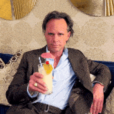 a man in a suit sits on a couch holding a drink