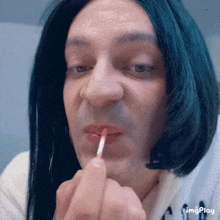 a man wearing a wig is applying lip gloss on his lips with a red brush