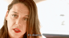 a woman with long hair and red lips is sitting in a car and says it 's diverse .