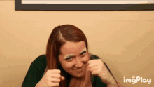a woman with red hair and white eyebrows is making a funny face with her fist in the air .