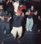 a group of people are dancing in a dark room and one of them is wearing sunglasses