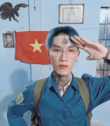 a man wearing glasses salutes in front of a flag with a yellow star