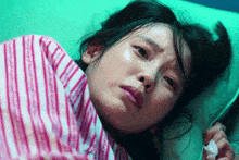 a woman in a pink and white striped shirt is laying down with her eyes closed