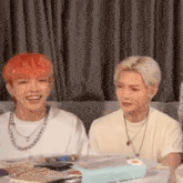 two young men are sitting at a table and smiling . one of the men has red hair .