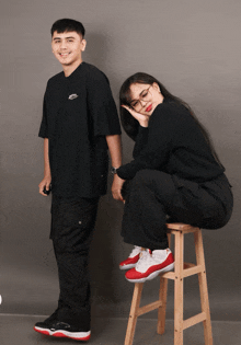 a man and a woman are posing for a picture and the woman is sitting on a wooden stool