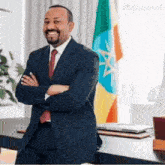 a man in a suit and tie is standing in front of a flag with his arms crossed and smiling .