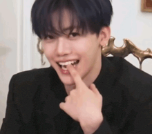 a young man in a black suit is holding his finger to his mouth