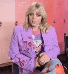 a woman wearing a purple jacket is sitting in front of a pink locker .