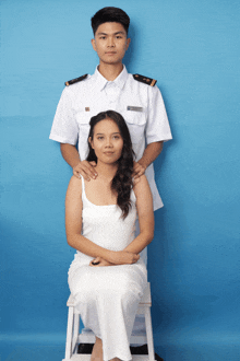 a man in a white uniform is standing next to a woman who is sitting on a stool