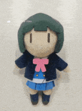 a stuffed doll with green hair and a pink bow sits on a white table