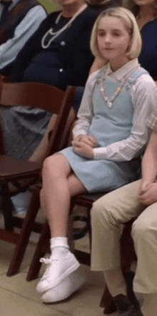 a girl in a blue dress is sitting in a chair with her legs crossed