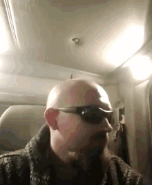 a bald man with a beard wearing sunglasses looks at the camera