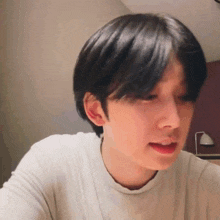 a young man with short black hair is making a funny face while sitting at a table .