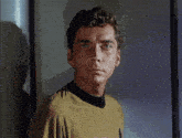 a man in a yellow shirt with a black collar is looking at the camera