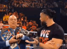 two men are standing next to each other in a wrestling ring . one of the men is wearing a we shirt .