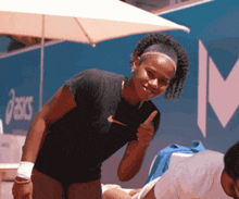 a woman giving a thumbs up in front of an asics sign