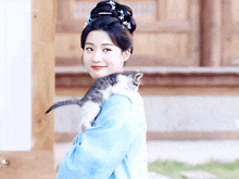 a woman in a blue dress holding a cat on her shoulder