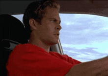 a man in a red shirt is driving a car .