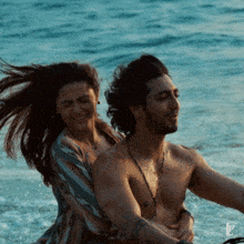 a shirtless man is being hugged by a woman in the ocean