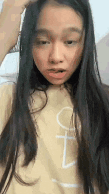 a young girl with long hair is making a funny face while wearing a yellow shirt .
