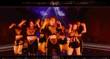 a group of women are dancing on a stage and one of them is making a gesture with her hand .