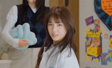 a girl in a white shirt looks at the camera while another girl holds a blue pillow