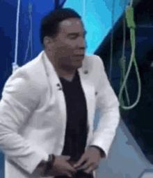 a man in a white suit and black shirt is standing in front of a rope hanging from a ceiling .