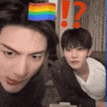 two young men are sitting next to each other in a room with a rainbow flag on their head .