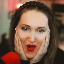 a woman with red lipstick is making a funny face while holding her face with her hands .