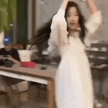 a woman in a white dress is standing in front of a table with her arms in the air .