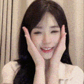 a woman with long black hair is smiling and holding her face with her hands .