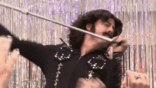 a man in a cowboy outfit is playing a violin in front of a tinsel curtain .