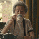 an elderly woman drinking from a white cup with a blue stripe