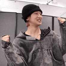 a man wearing a black beanie and a grey jacket has a name tag that says ' hongma ' on the front