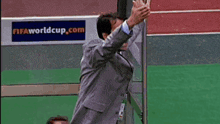 a man in a suit is jumping in the air in front of a worldcup.com sign