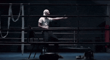 a man in a white shirt is standing in a boxing ring behind a chair