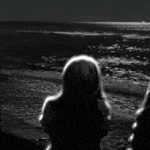 a black and white photo of two people looking at the ocean at night
