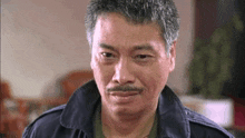 a man with a mustache is wearing a blue jacket and making a funny face .